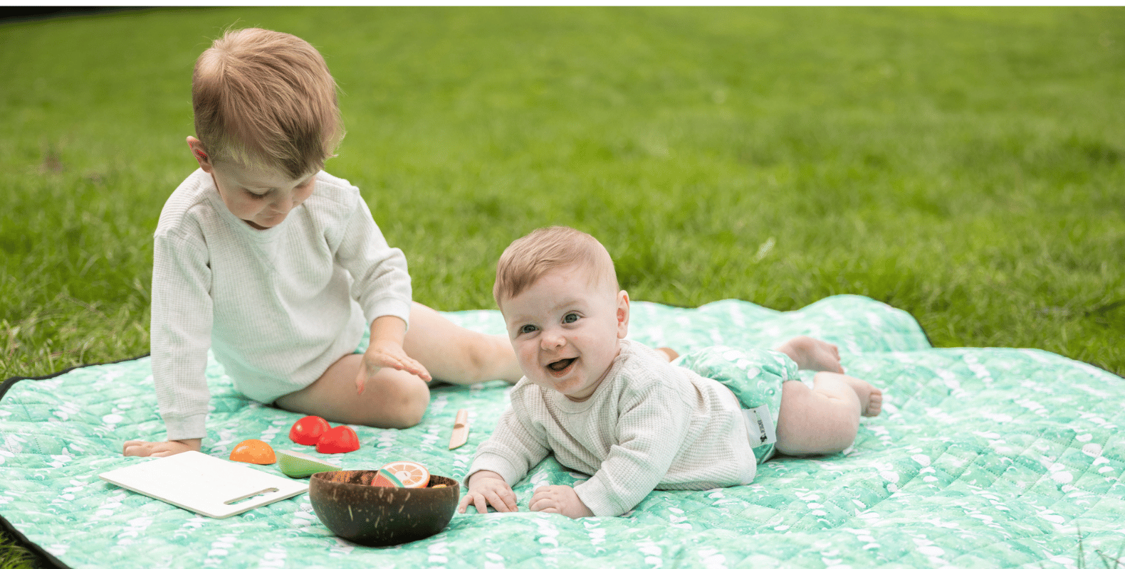 A baby and toddler on a play mat in cloth nappies